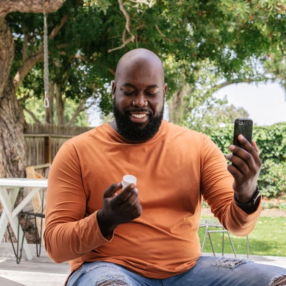 Man holding 9amHealth medication vial and phone in his hands